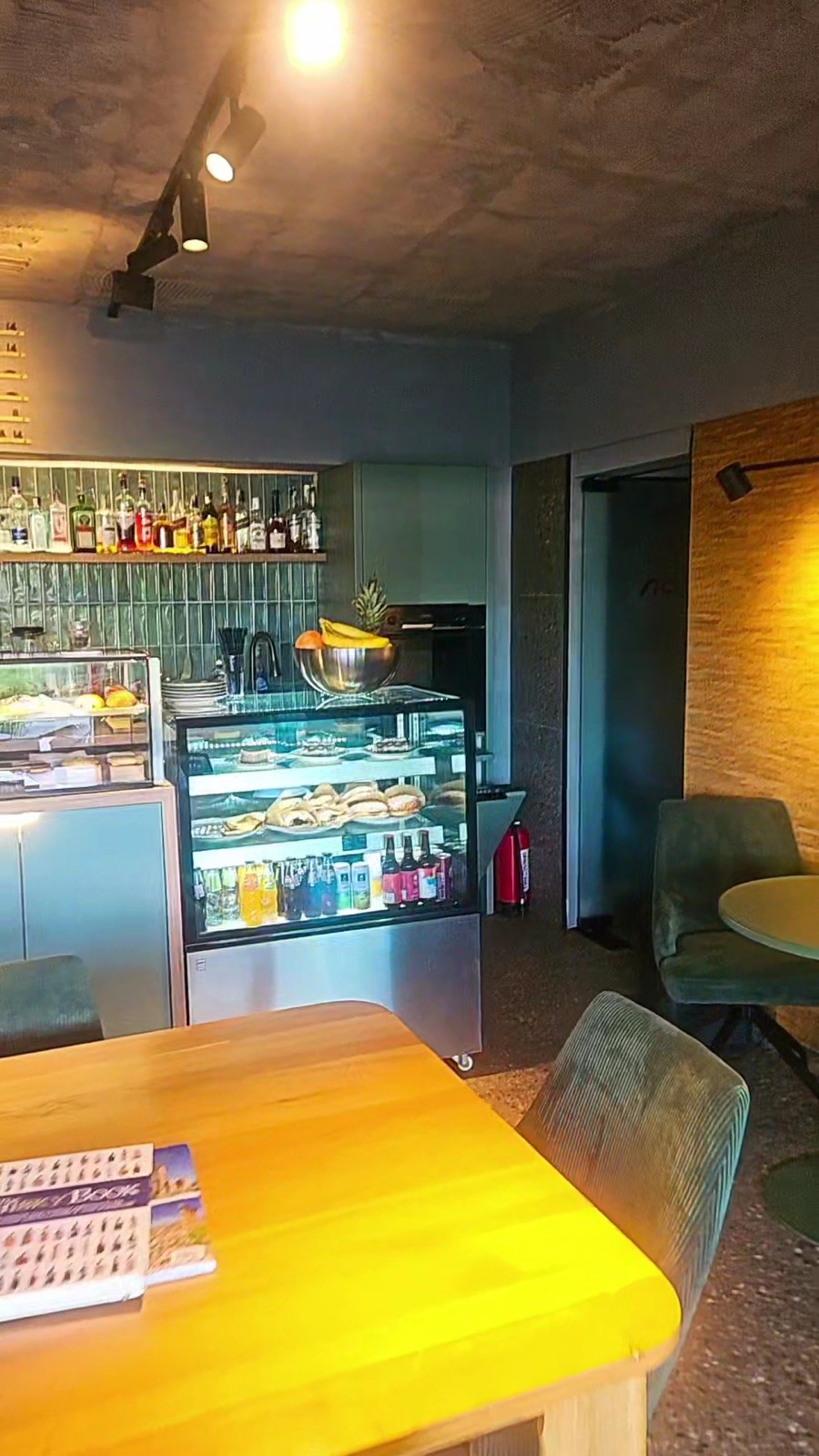 Interior noi², cu mese de lemn, scaune verzi și vitrina cu deserturi